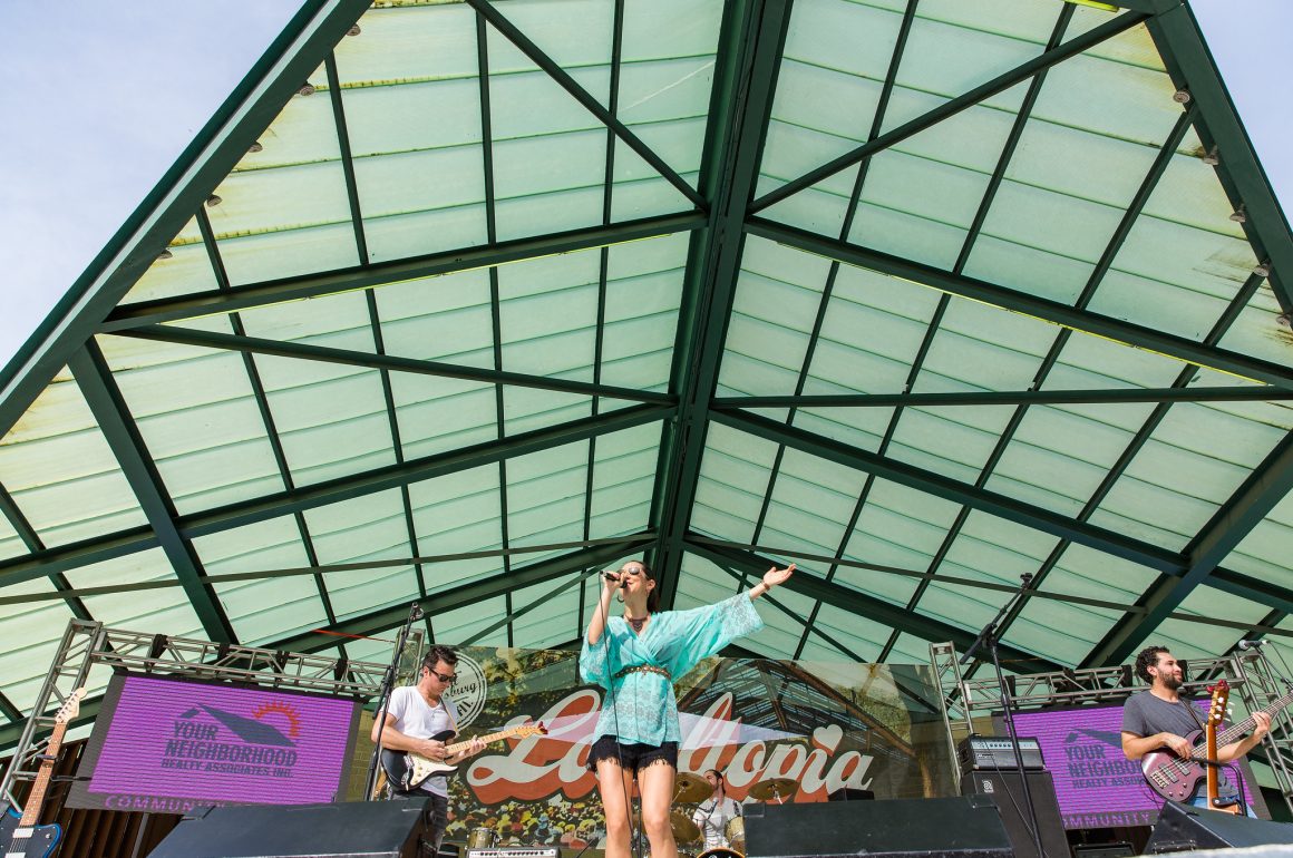 A photo of a band on an outdoor stage with a large, triangular roof.