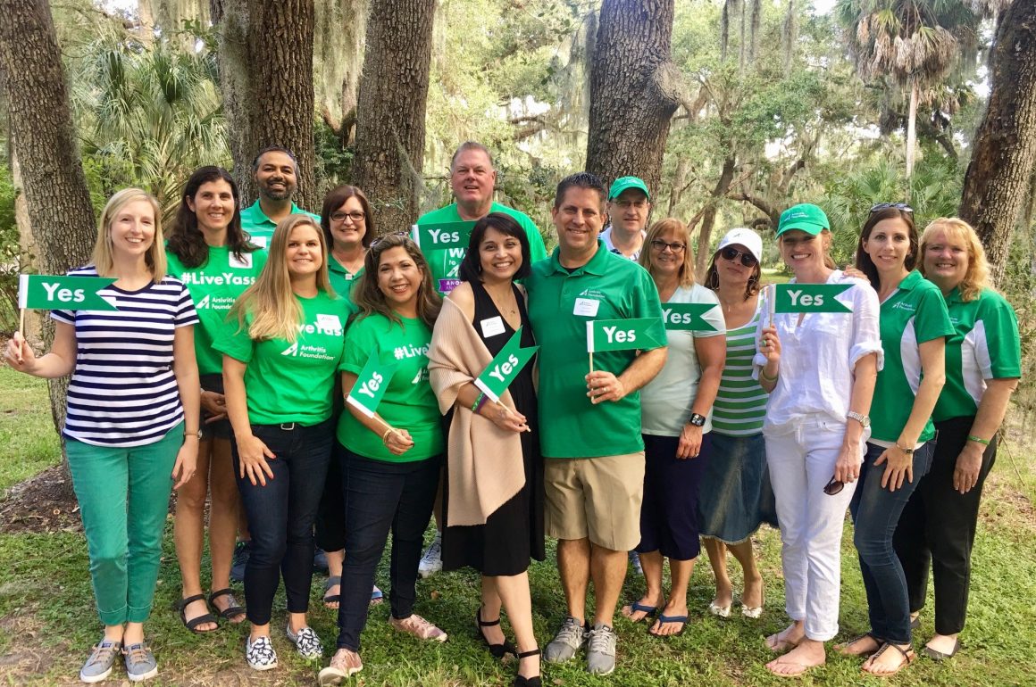 A photo of a group of people posing for a photo outside, many dressed in green t-shirts.