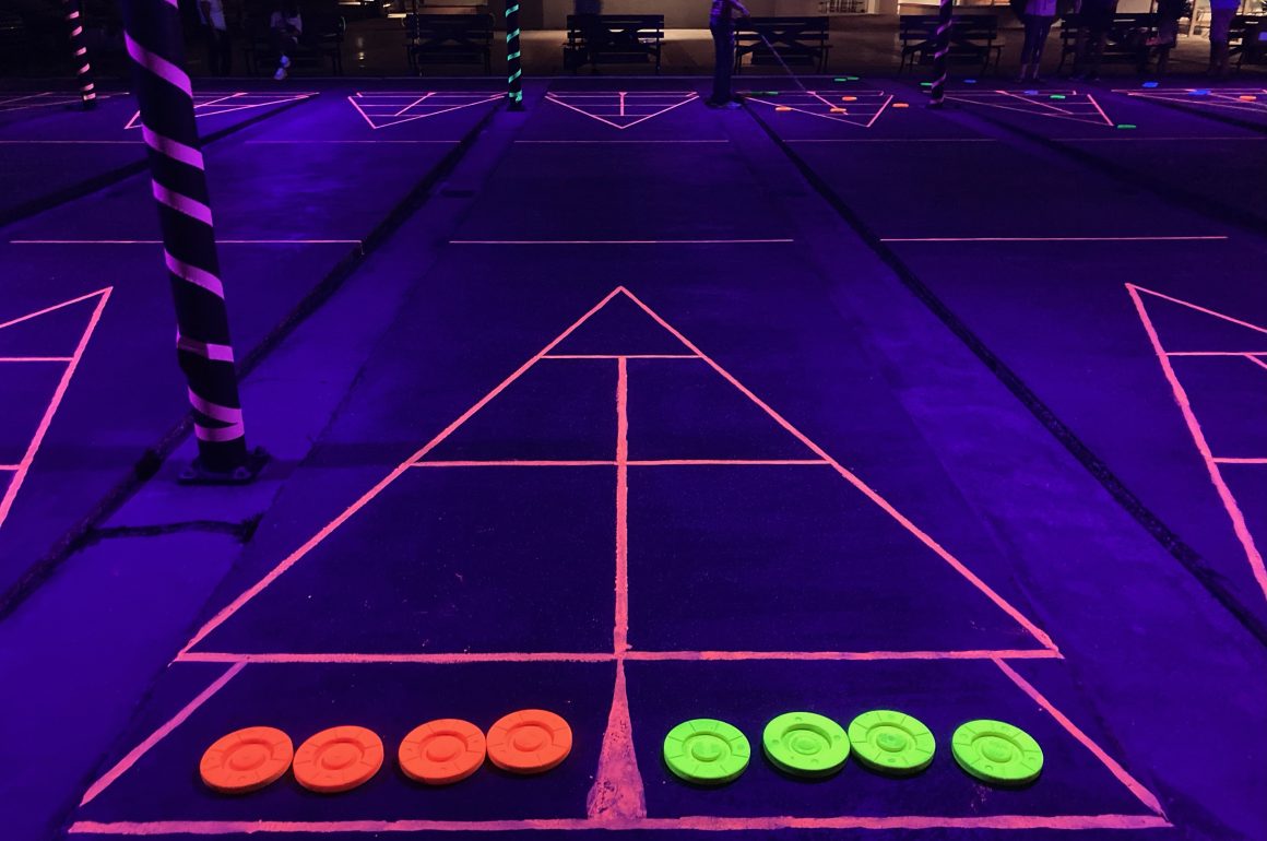 A photo of black-lit shuffleboard courts at night.